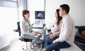 Doctor talking with pregnant couple, sonogram displayed on monitor